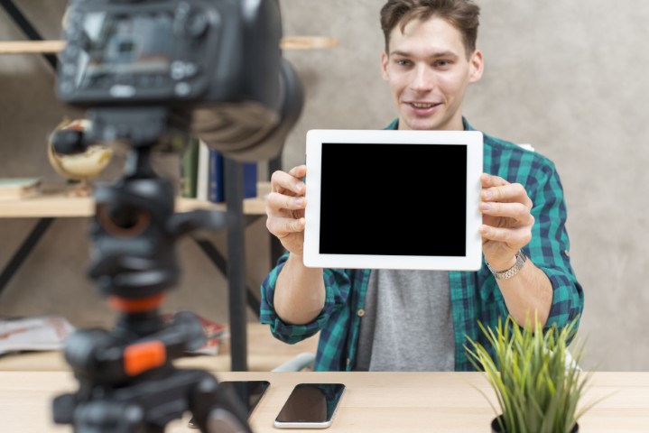 Vlogger talking to the camera while holding a tablet, showing where the scrolling script will be read from